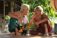 A relexed elderly couple sitting on a deck sharing a bowl of fruituit